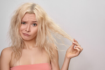 Beautiful woman with messed up hair. Unhappy grimacing face. Blond bleaching hairstyle with problem brittle hair - obrazy, fototapety, plakaty