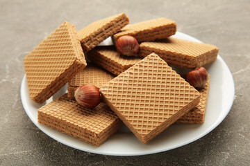 Square chocolate wafer biscuits with hazelnut on white plate on grey background.