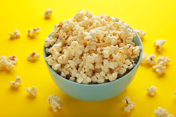 Fresh popcorn in blue bowl on yellow background.