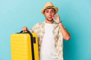 Young caucasian man going to travel isolated on blue background  with fingers on lips keeping a secret.