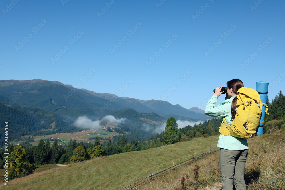 Sticker tourist with hiking equipment looking through binoculars in mountains