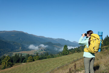 Fototapeta na wymiar Tourist with hiking equipment looking through binoculars in mountains