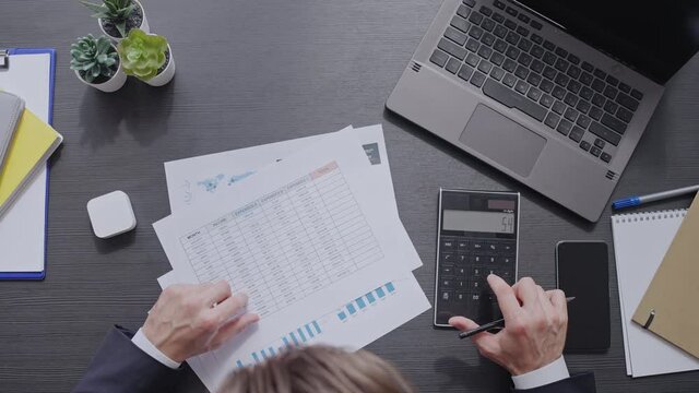 Male accountant counting numbers, calculating total amount on calculator