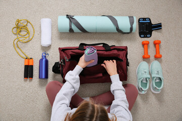 Woman packing sports stuff for training into bag on floor, top view