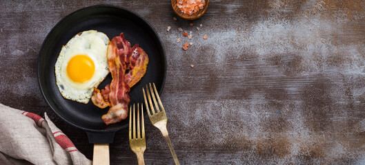 Traditional English breakfast with fried eggs and bacon in cast iron pan on dark concrete...