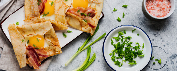 Crepe with fried egg, cheese, bacon and green onions for breakfast on a light gray concrete background