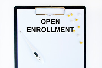 On the tablet for writing, the text OPEN ENROLLMENT is marked, as well as yellow tablets and a thermometer on it.