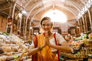 Young indian woman making namaste gesture during sopping in eastern market