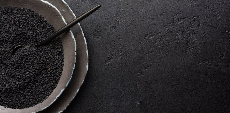 Black sesame seeds in black ceramic plates on a dark old vintage background. Rustic style. Top view