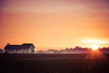 I farmhouse and field at sunrise with a slight morning mist in Indiana.