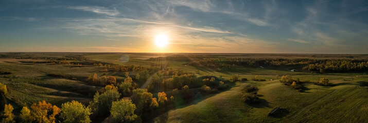 Aerial panorama of a sunset over the gentle rolling hills of the Great Plains with trees in their...