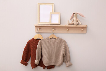 Wooden shelf with child's clothes, toy bunny and photo frames on beige wall. Interior element