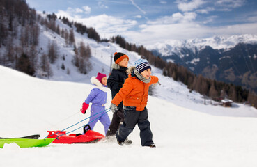 childhood, sledging and season concept - group of happy little kids walking, with sleds in winter...