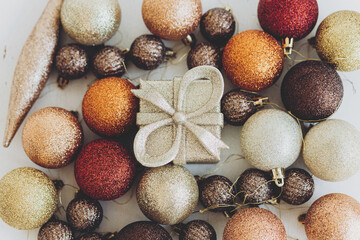 Small Christmas gift box near Christmas ornaments flat lay, Top view of Christmas decorations, glitter balls and golden toys on white background