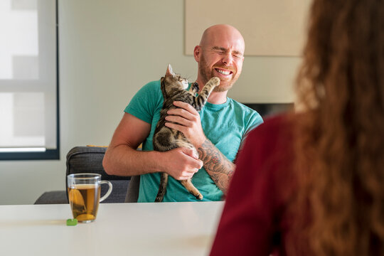 Happy man holding cat with woman at table