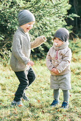 Outdoor portrait of little preschool brother trying to cheer up shy toddler sister