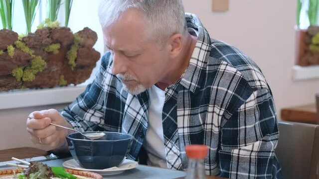 Close-up of an elderly man with a beard enjoying hot Asian soup at lunch in a restaurant. The concept of Vietnamese cuisine.