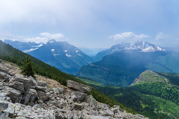 View of Lake McDonald from a distance through the clouds and trees in Glacier National Park, as viewed from hiking on the Highline Trail by the Going to the Sun Road on a sunny summer day