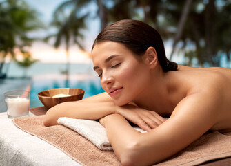 wellness, beauty and relaxation concept - young woman lying at spa over tropical beach background...