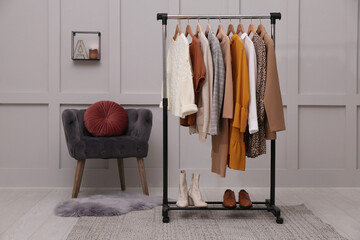 Rack with different stylish clothes and shoes near grey wall in room