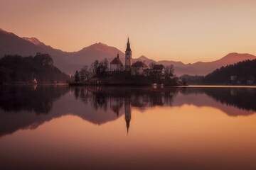 Fototapeta na wymiar Picturesque sunrise on the lake Bled. Perfect reflection of the church in smooth water. Atmospheric mood. Nature background. The nature of Slovenia. Lake Bled.Parish Church of St. Martina. Europe