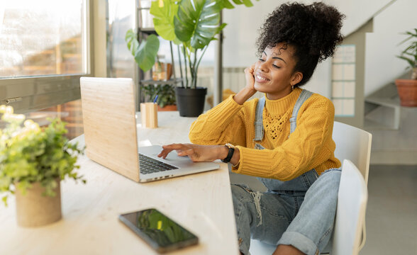 Smiling curly haired woman using laptop at home