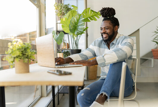 Hipster man laughing and using laptop at home