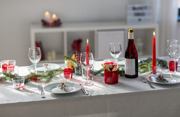 winter holidays, dinner party and celebration concept - christmas table serving with candles, crockery and wine at home