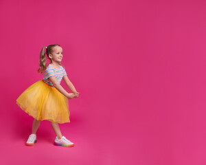 Cute little girl in tutu skirt dancing on pink background. space for text