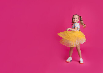 Cute little girl in tutu skirt dancing on pink background. space for text