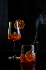 Aperol cocktail , two glasses of cocktail on a black background with ice cubes and orange slices . Bar or restaurant content .