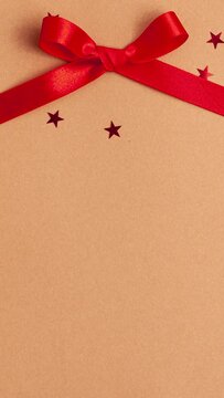 Red satin ribbon bow that tied on brown background with red stars shapes. Stop motion vertical animation Christmas Holidays and presents concept flat lay with copy space