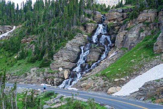 A man looks at Oberlin Falls, a waterfall on the Going to the Sun Road in Glacier National Park in Montana on a sunny summer evening at golden hour