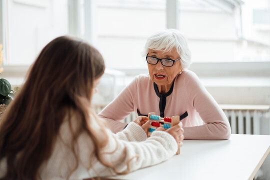 Senior woman talking to girl with abacus at table