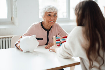 Grandmother showing piggy bank to granddaughter at table