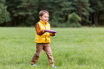 childhood, leisure and people concept - happy little boy playing game with flying disc at park