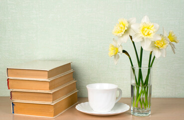 Daffodils, a white cup and saucer, books. Concept reading, classic literature. Place for text, copy space