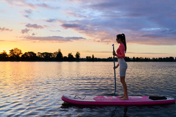 Active young woman with brown hair practicing in swimming on sup board with paddle with summer...