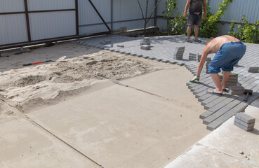 A worker is laying paving slabs in the yard. Construction