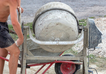 A worker works with a concrete mixer at a construction site.