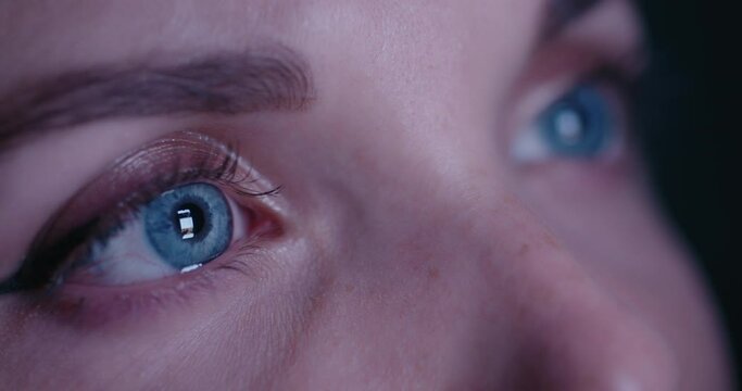 Extreme close up macro of beautiful woman blue eyes addicted by social network, looks into a smartphone screen with fast flickering social network feed, posts. Blinking screen reflection in eyes