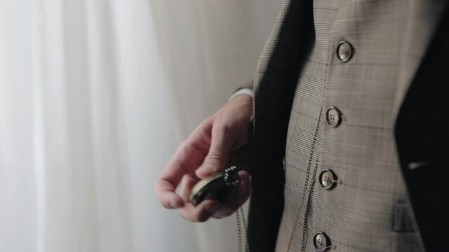 The man holds a watch on a chain in his hand and after checking the time puts it in his pocket. Close-up shooting