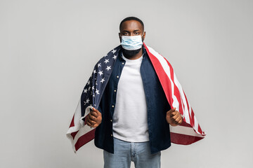 Confident serious African American fighter for rights man covered with USA flag, protect himself...