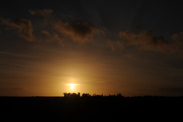 Sunset at dusk in the evening with trees, clouds and orange sky in Normandy, northern France