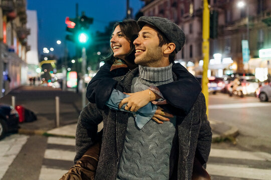 Happy man carrying girlfriend piggyback on city street
