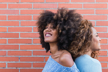 Side view of smiling african american women with long afro hair and glamour makeup posing in brick wall. Beauty portrait of african natural girls standing back to back with copy space