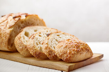 Sliced freshly traditional wheat bread on wooden board on light background, selective focus.