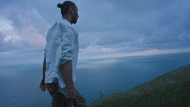Young attractive handsome stranger traveler man walking through beautiful wheat field in windy north sea landscape with bag in his hand. Cinematic fashion advertisement freedom concept shot