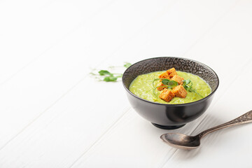 Green peas soup with breadcrumbs in a bowl on a white wooden table. Copy space