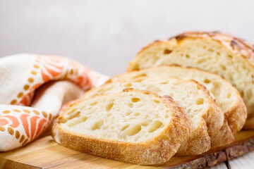 Sliced freshly homemade wheat bread on wooden board on light background, selective focus.